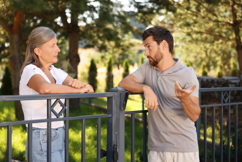 emotional-neighbours-having-argument-near-fence-outdoors-