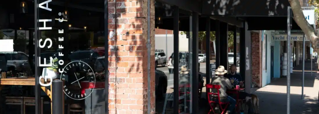 Exterior of GESHA Coffee Co in Fremantle with red outdoor seating and people enjoying coffee on the footpath.
