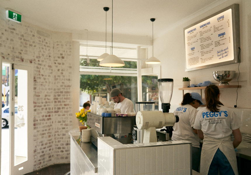 Interior of Peggy’s Sandwich Servery in Fremantle with staff preparing coffee behind a white-tiled counter and menu board on the wall.