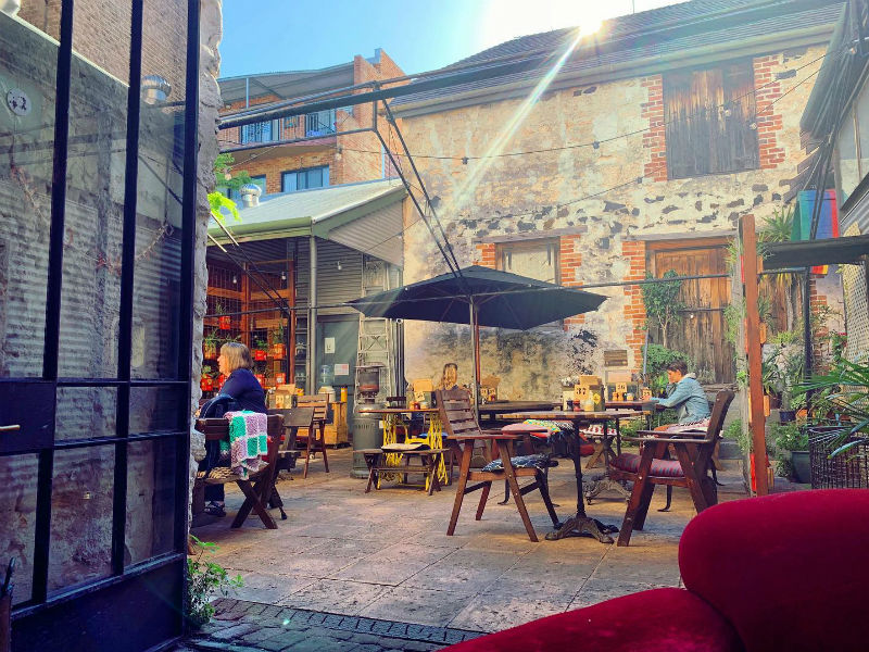 Courtyard seating at Moore & Moore Café in Fremantle with rustic stone walls, wooden furniture, and umbrellas on a sunny day.